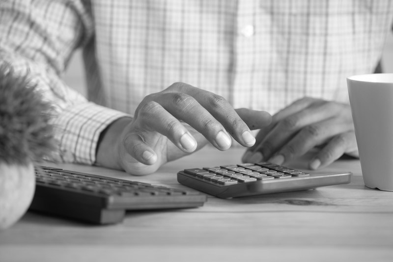 Dos manos hacen cuentas en una calculadora junto a un teclado y una taza