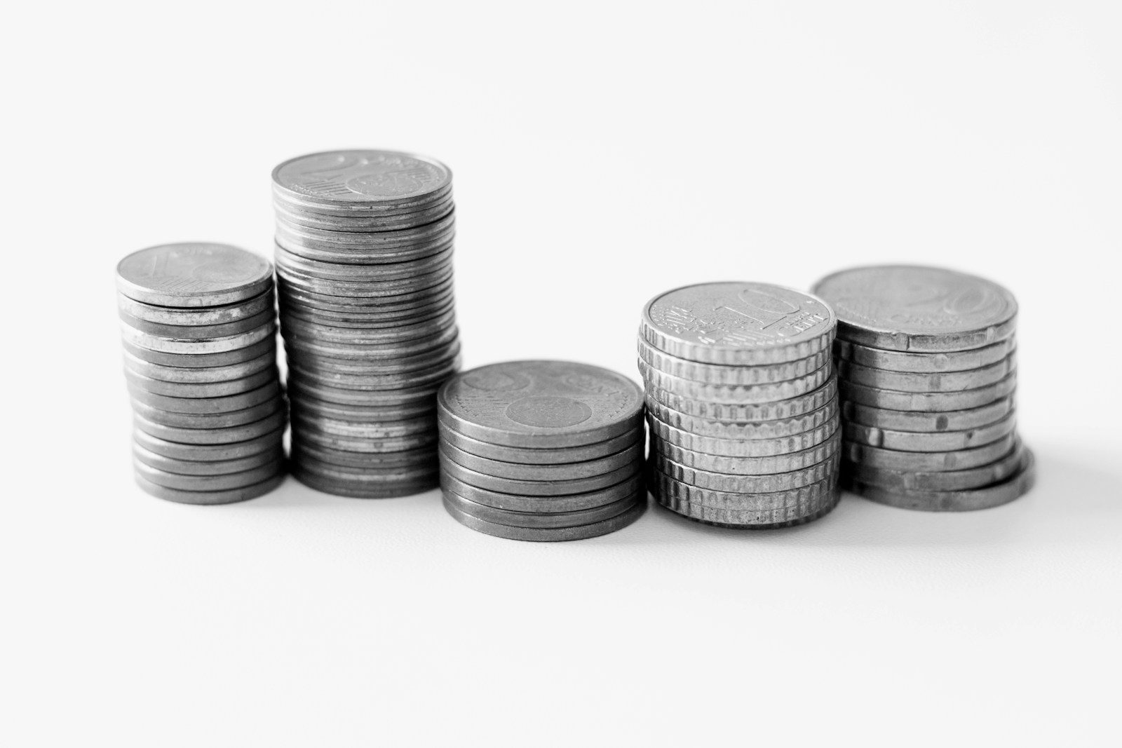Cinco pilas de monedas de distintas alturas sobre una mesa blanca