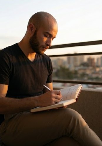 Carlos Alberto Cardona B. escribiendo en un cuaderno en un balcón de Bogotá al atardecer